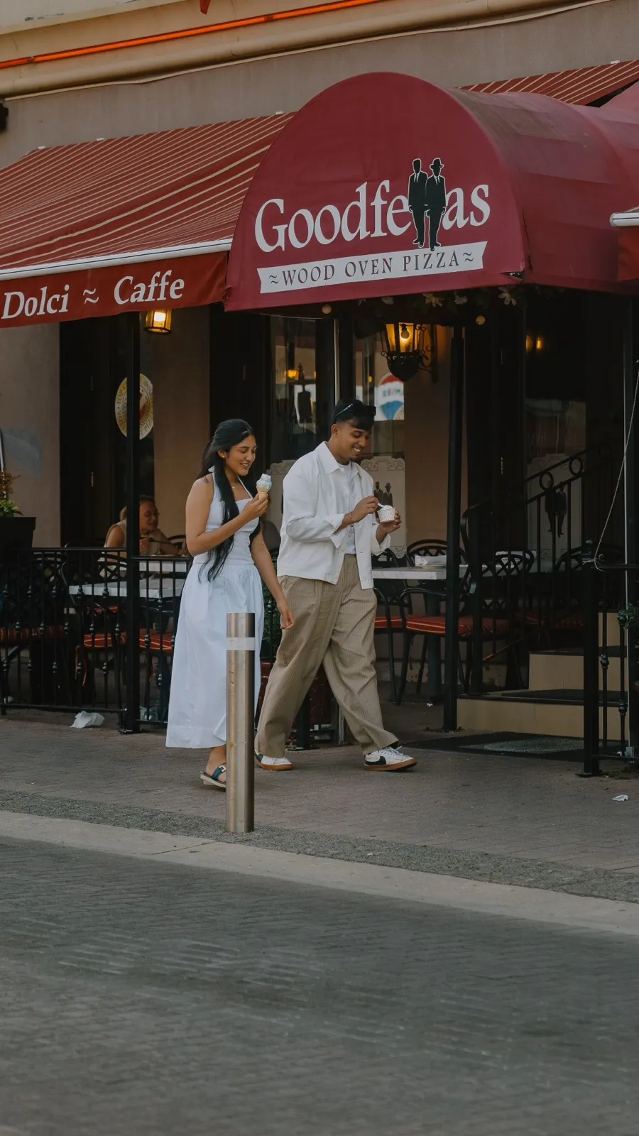 Dev and his sister walking past the Goodfellas Wood Oven Pizza patio with ice cream