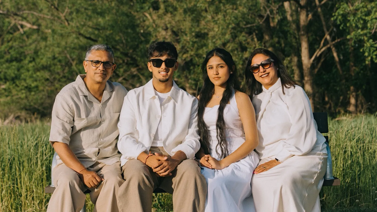 Dev with his father, mother, and sister on a bench in a field at golden hour