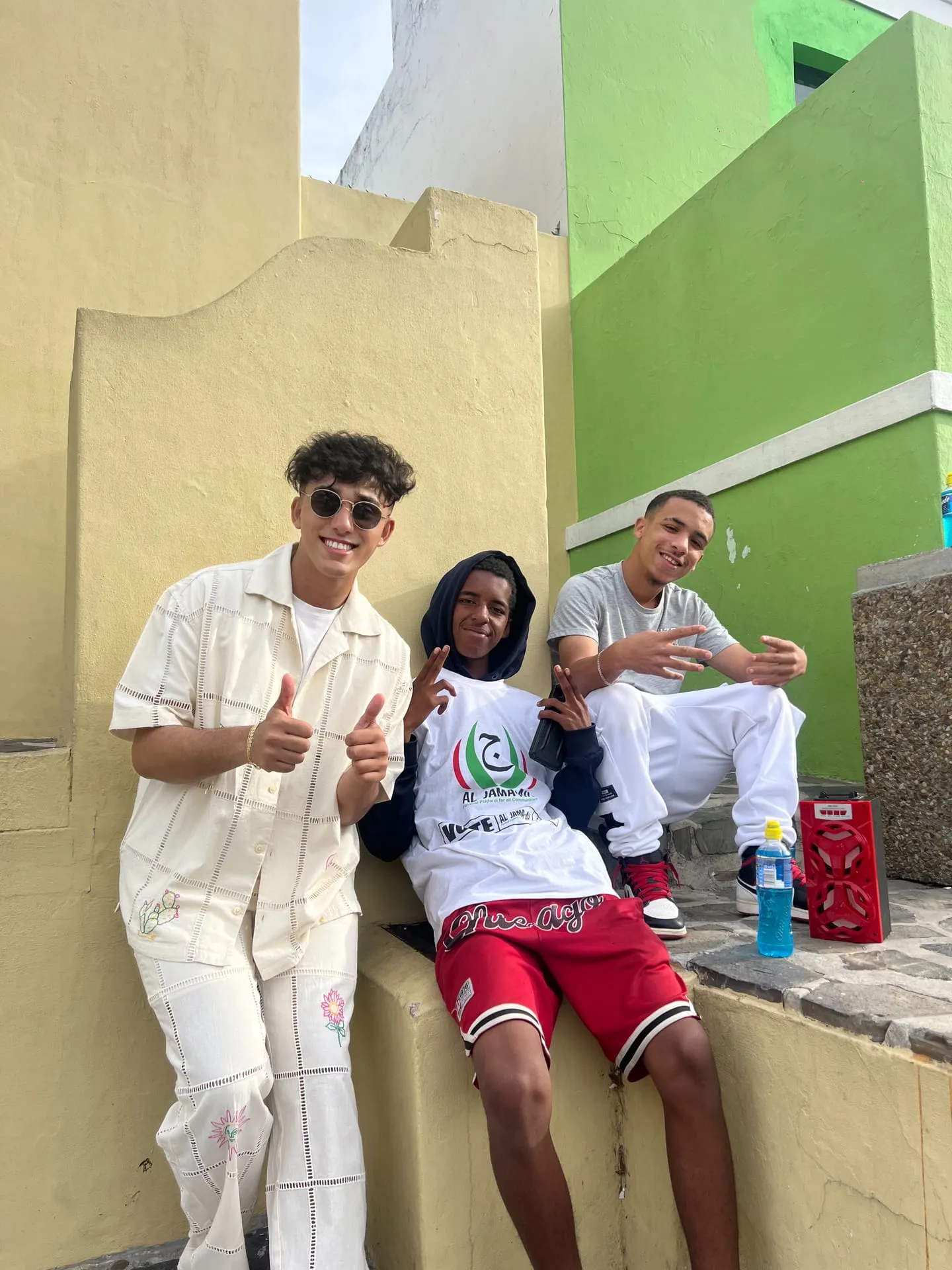 Dev Vashi smiling with two young people, all giving thumbs up and peace signs